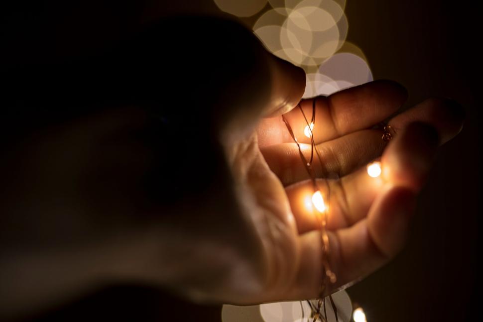 Hands gently holding warm lights, symbolising comfort, hope and support for someone who is grieving.
