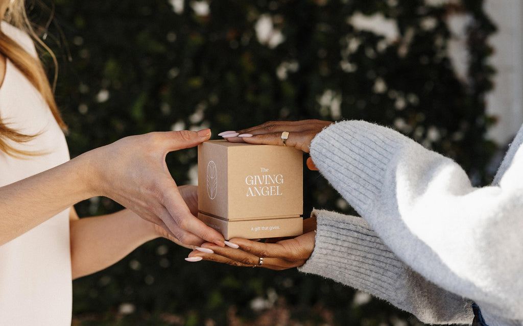 Hands exchanging a The Giving Angel gift box, symbolising meaningful giving and human connection.